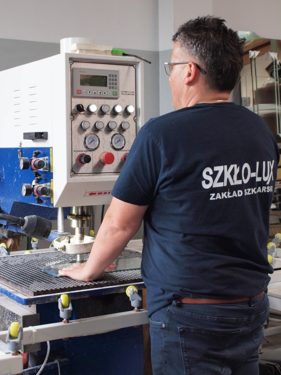 pracownik przy paszynie do obróbki CNC, wykonujacy otwór w szkle